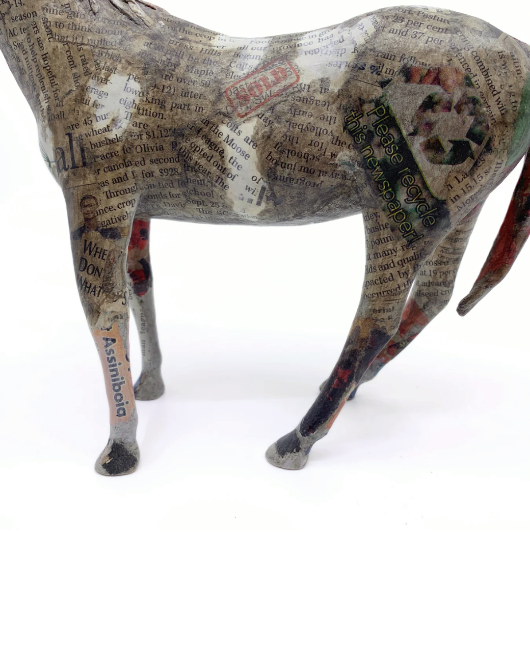 A sculptural horse figurine decorated with collage elements, including newspaper print, text, and small printed images, shown against a plain white background.