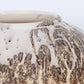 A round ceramic vessel. Surface is textured, with beige, tan, and brown crackly splotches.