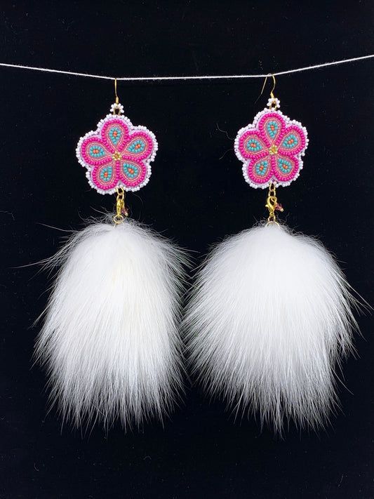 A pair of long dangle earrings with pink and turquoise beaded flower charms and large white faux fur tassels, hanging from a thin white string against a black background.