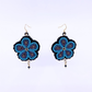 A pair of handmade beaded dangle earrings with a five-petal flower design in bright blue, purple, and black, hanging from gold-tone fishhook wires on a white background.