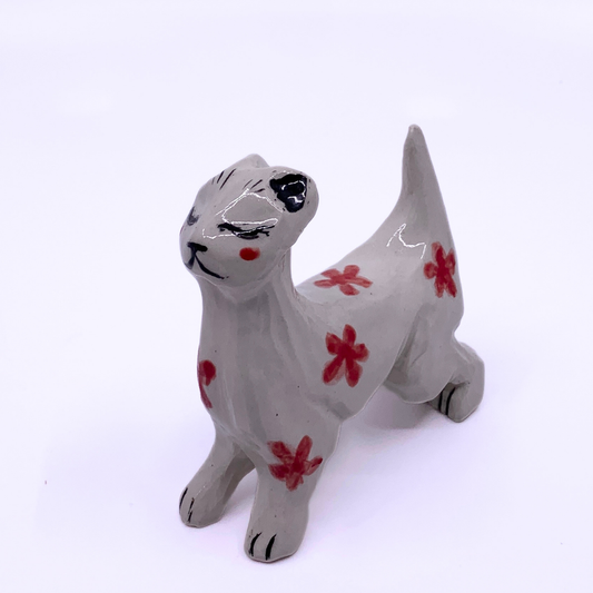 A small ceramic cat figurine in light gray with hand-painted red flowers and black facial details, photographed on a plain white background.