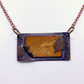 A rectangular pendant necklace with a copper-toned chain, featuring a central textured gold-toned panel with embossed floral details and a dark brown-grey border.