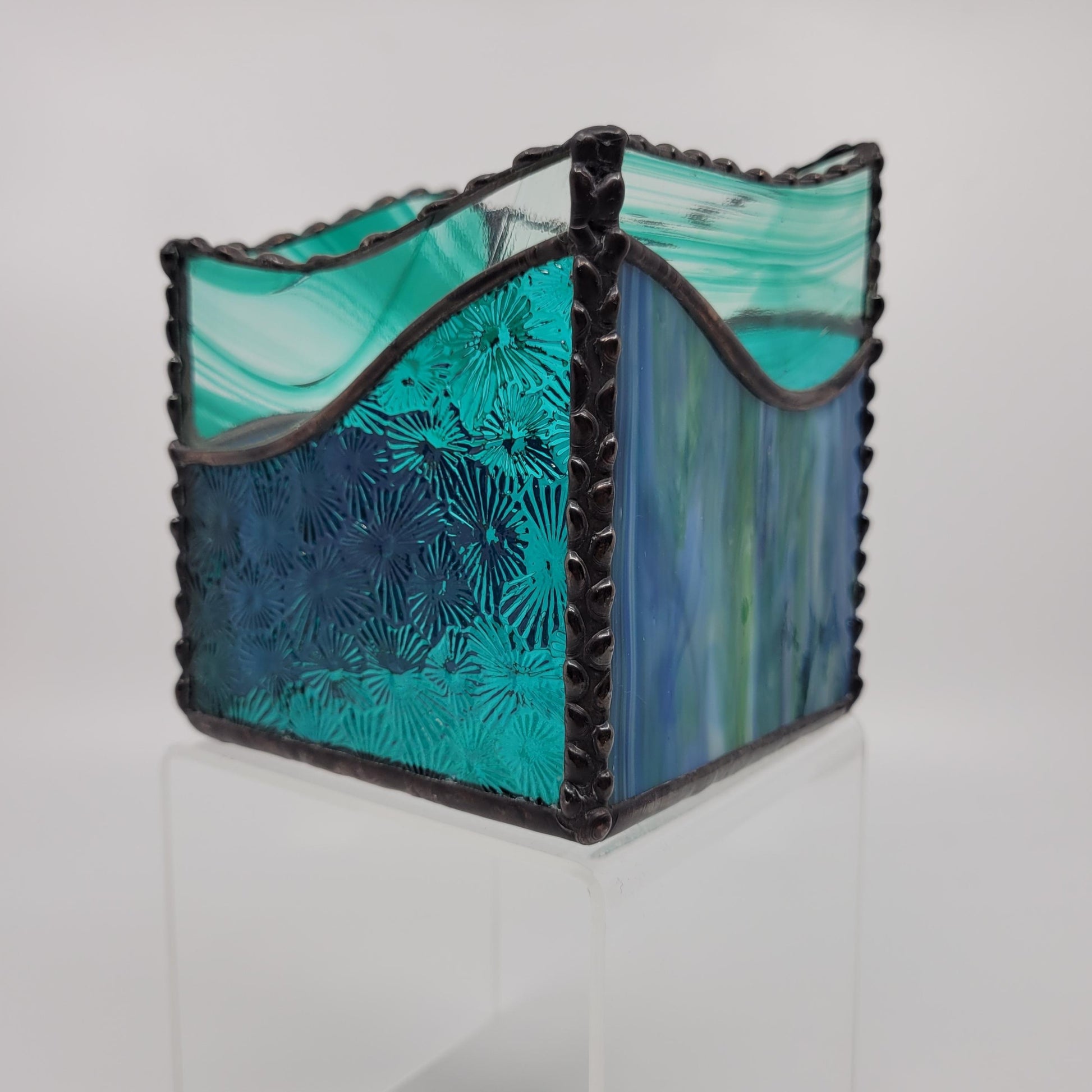 A square decorative box with a black scalloped frame and panels of turquoise, teal, and blue marbled glass