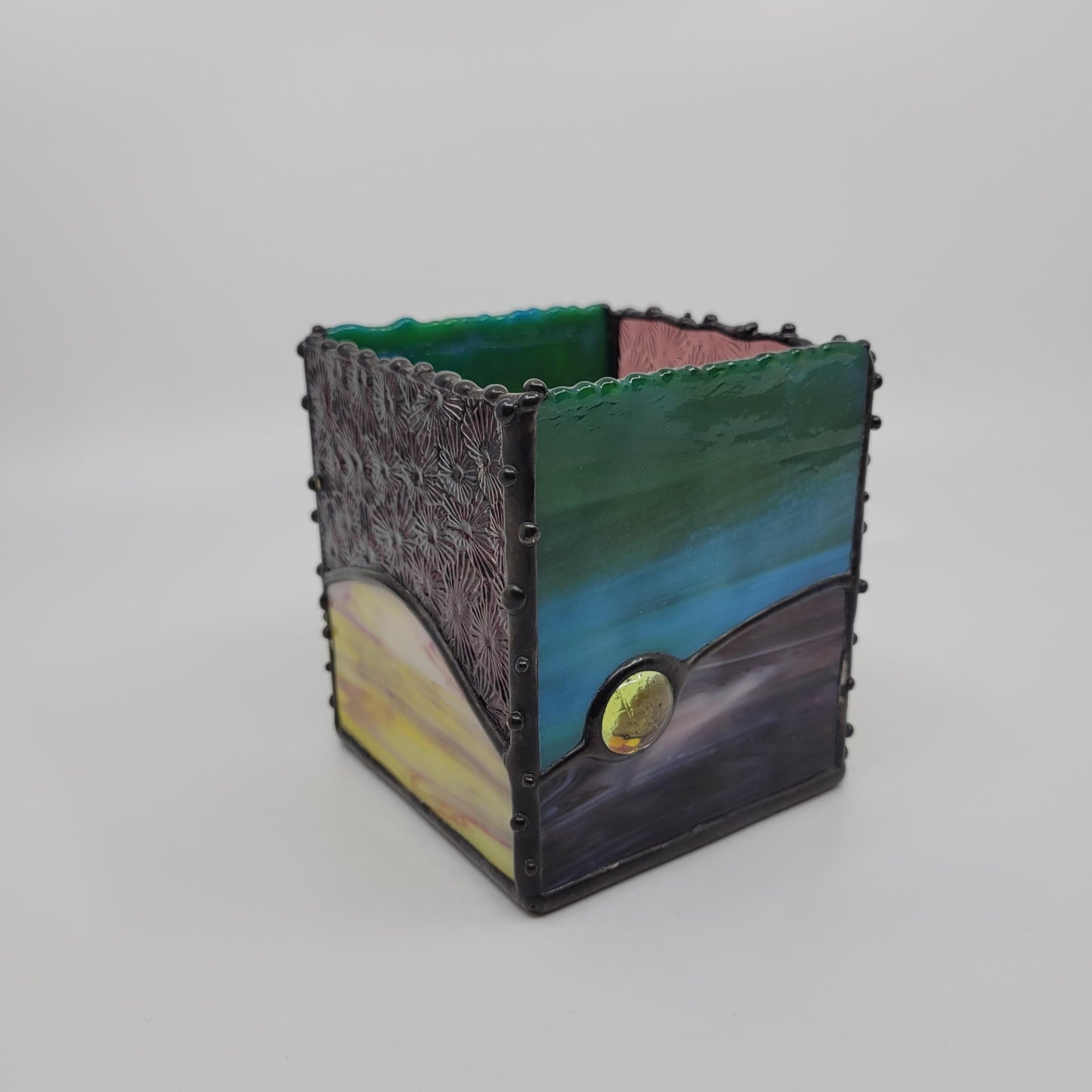 A small decorative box with green, blue, yellow, and purple hues, framed by a dark metallic border with rivet details.
