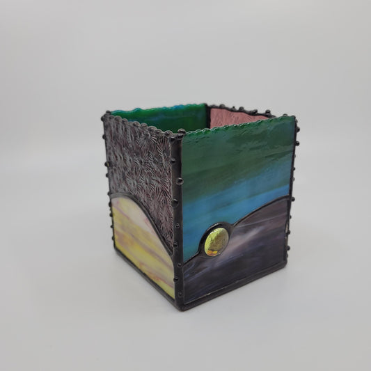 A small decorative box with green, blue, yellow, and purple hues, framed by a dark metallic border with rivet details.