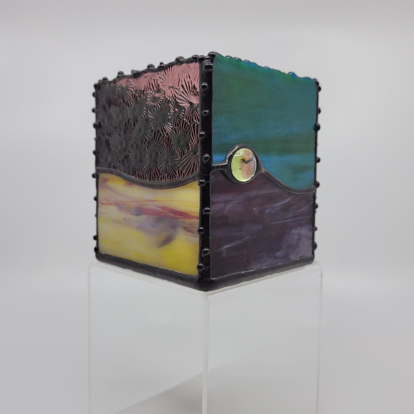 A small decorative box with green, blue, yellow, and purple hues, framed by a dark metallic border with rivet details.