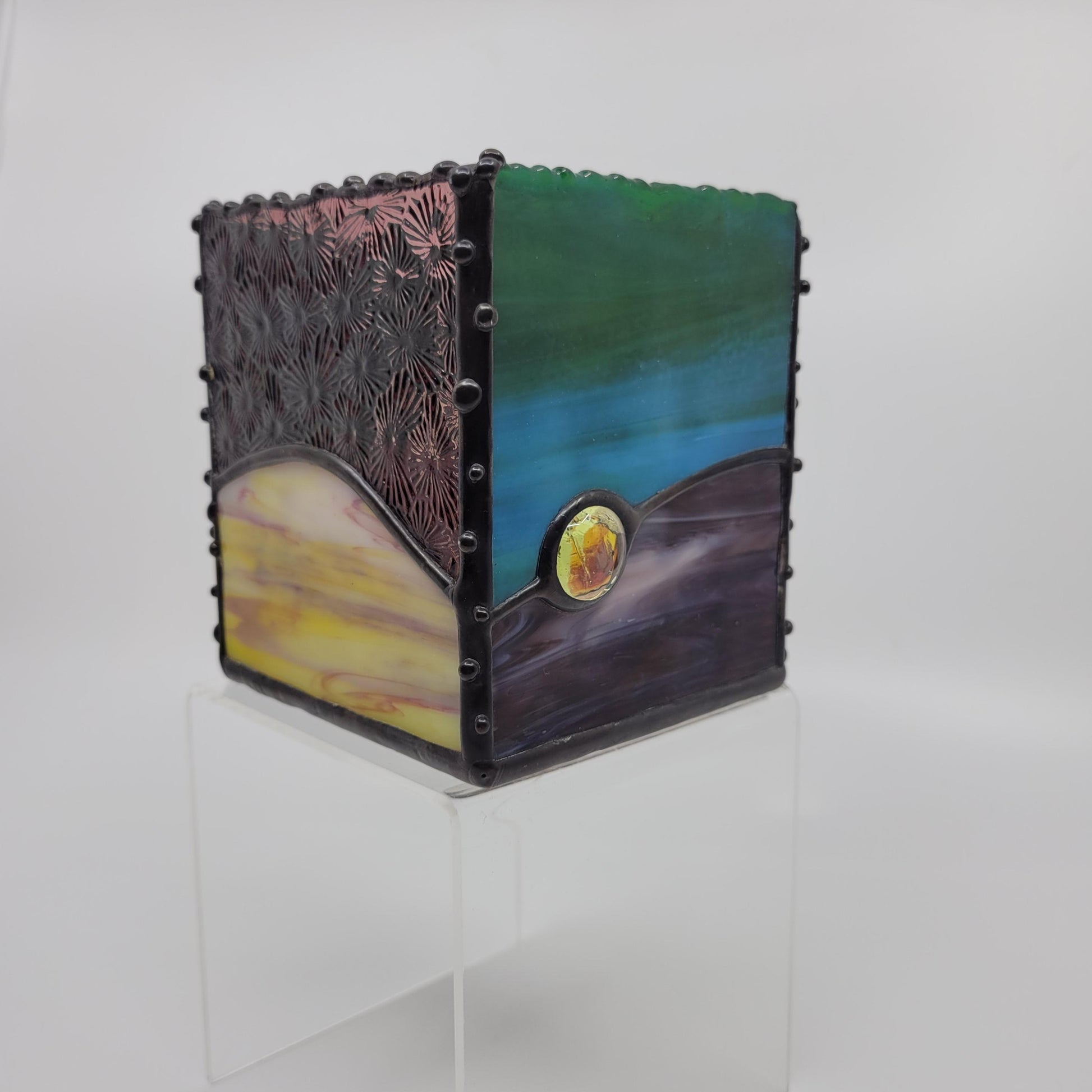A small decorative box with green, blue, yellow, and purple hues, framed by a dark metallic border with rivet details.