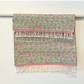 Pink and Green woven rug with fringe hanging over a bar 