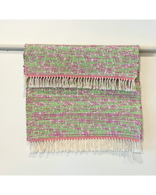 Pink and Green woven rug with fringe hanging over a bar 