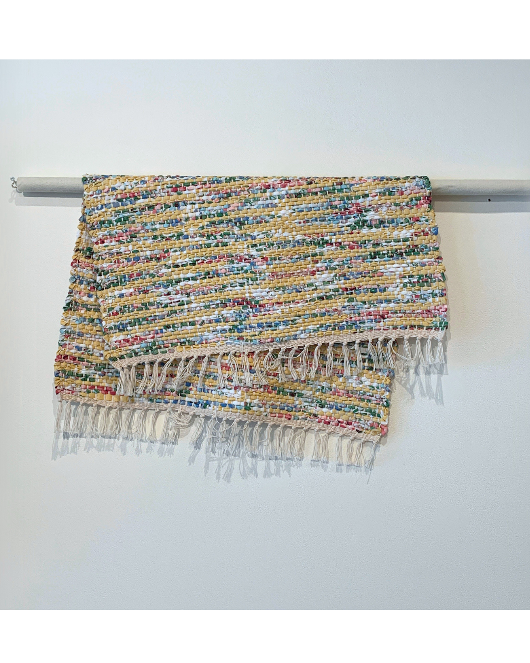 Colourful woven rug with fringe hanging over a bar