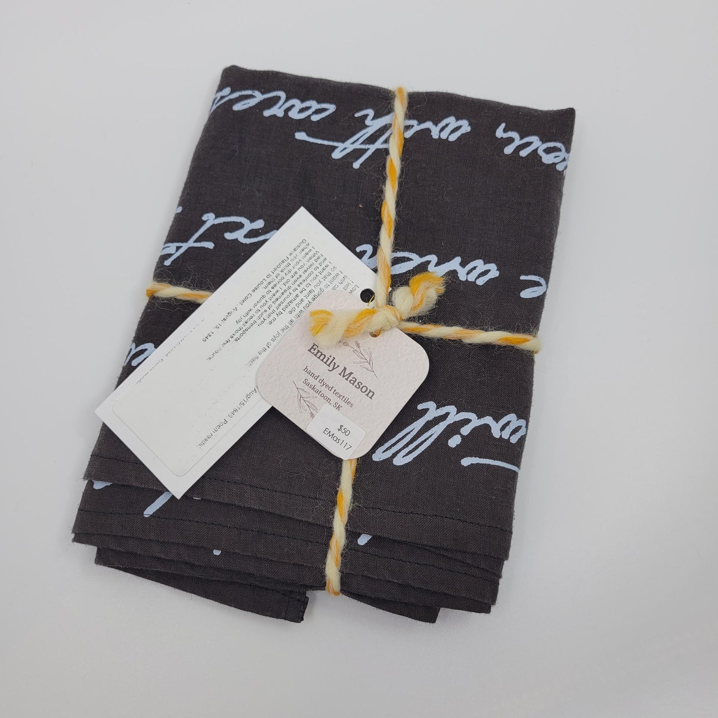 Stack of black fabric napkins with white text, tied with yellow string, on a light gray background.