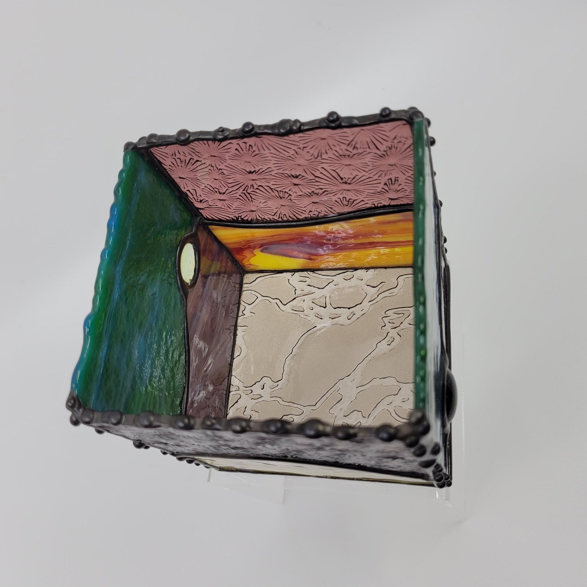 Interior view of a small decorative box with green, blue, yellow, and purple hues, framed by a dark metallic border with rivet details.