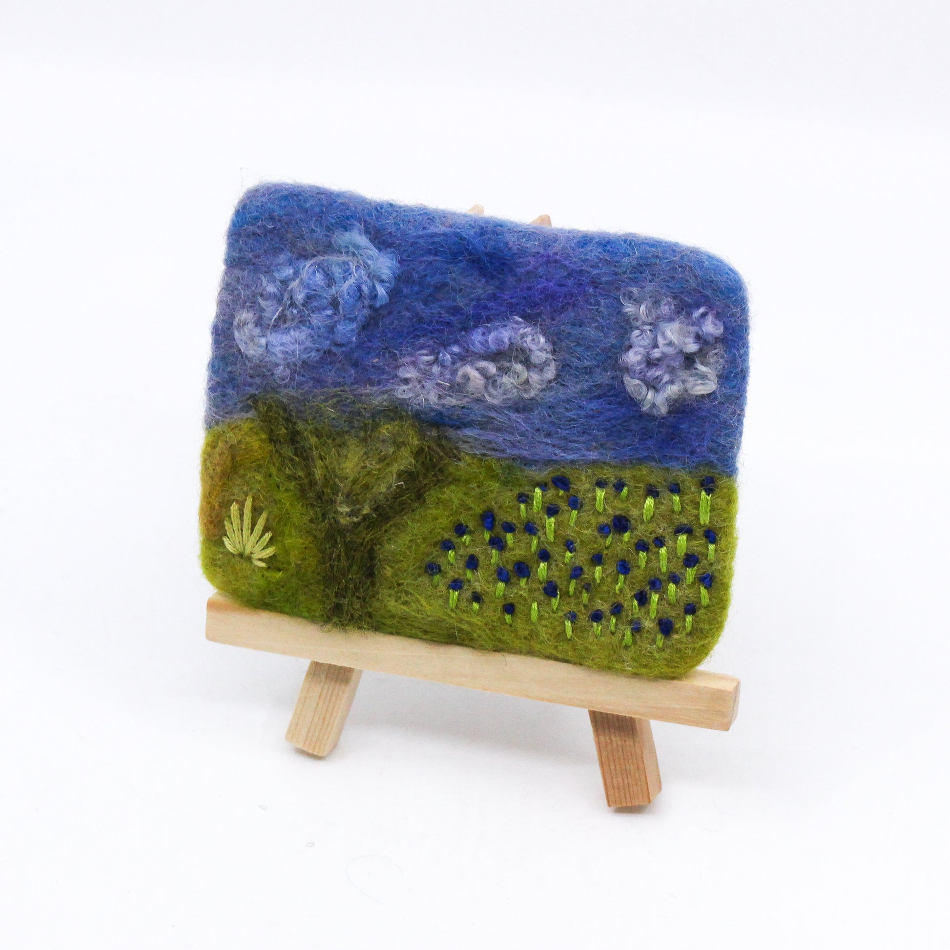 Felted landscape of blue flowers on wooden easel