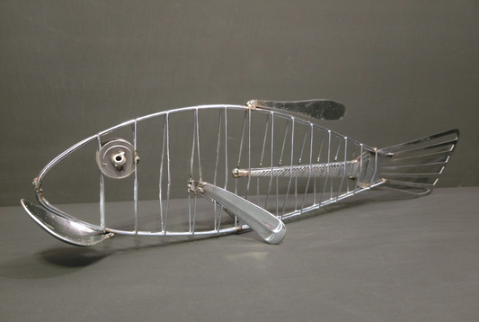 Metal fish made from repurposed cutlery, silver in colour, on grey background