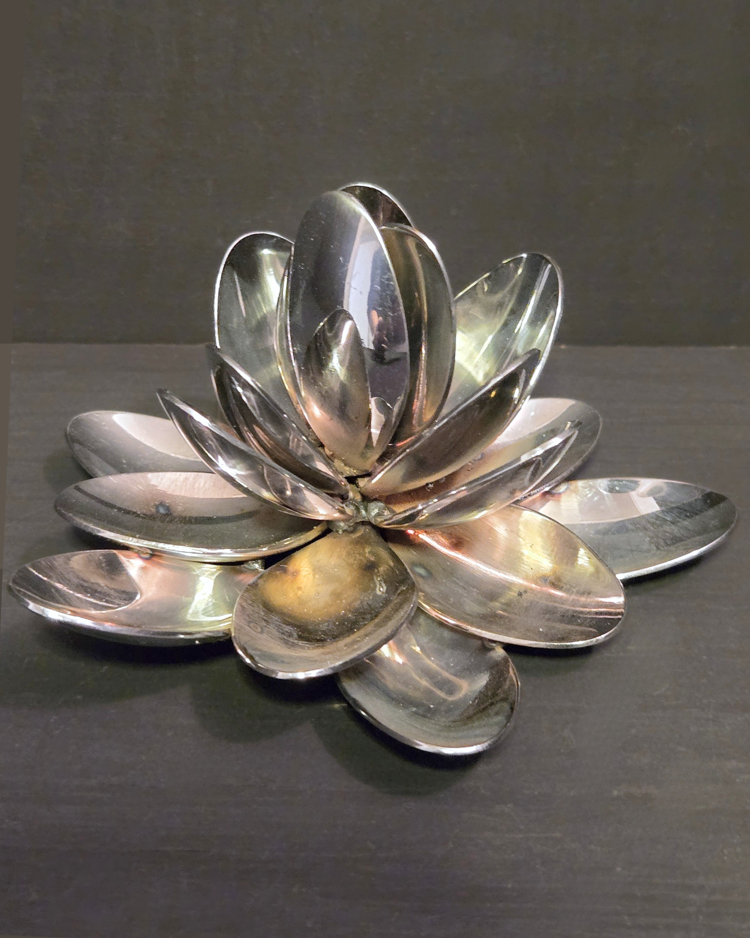 Lotus flower sculpture made with repurposed spoons, silver in colour, on grey background