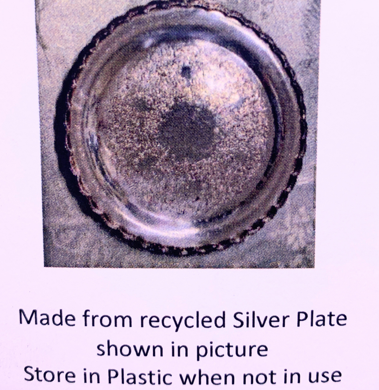 A round tarnished silver plate with a scalloped rim, shown on a light background with text below stating it is made from recycled silver plate.