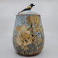 Ceramic jar with floral design and bird on lid against a white background