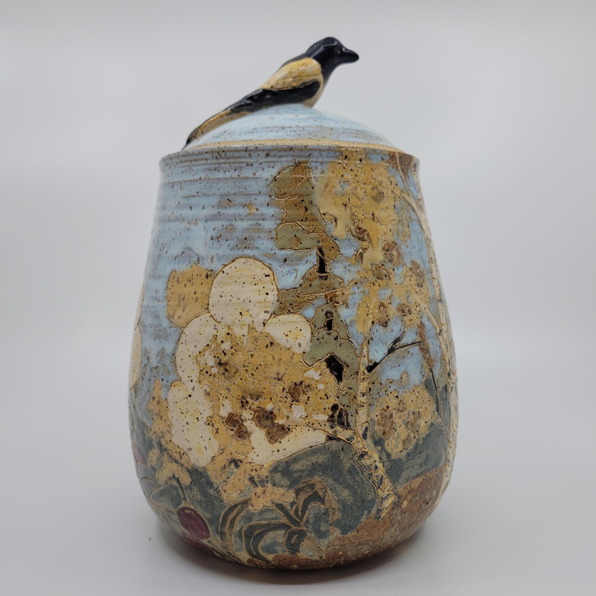Ceramic jar with floral design and bird on lid against a white background