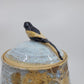 Ceramic jar with a lid featuring a bird sculpture on a plain background