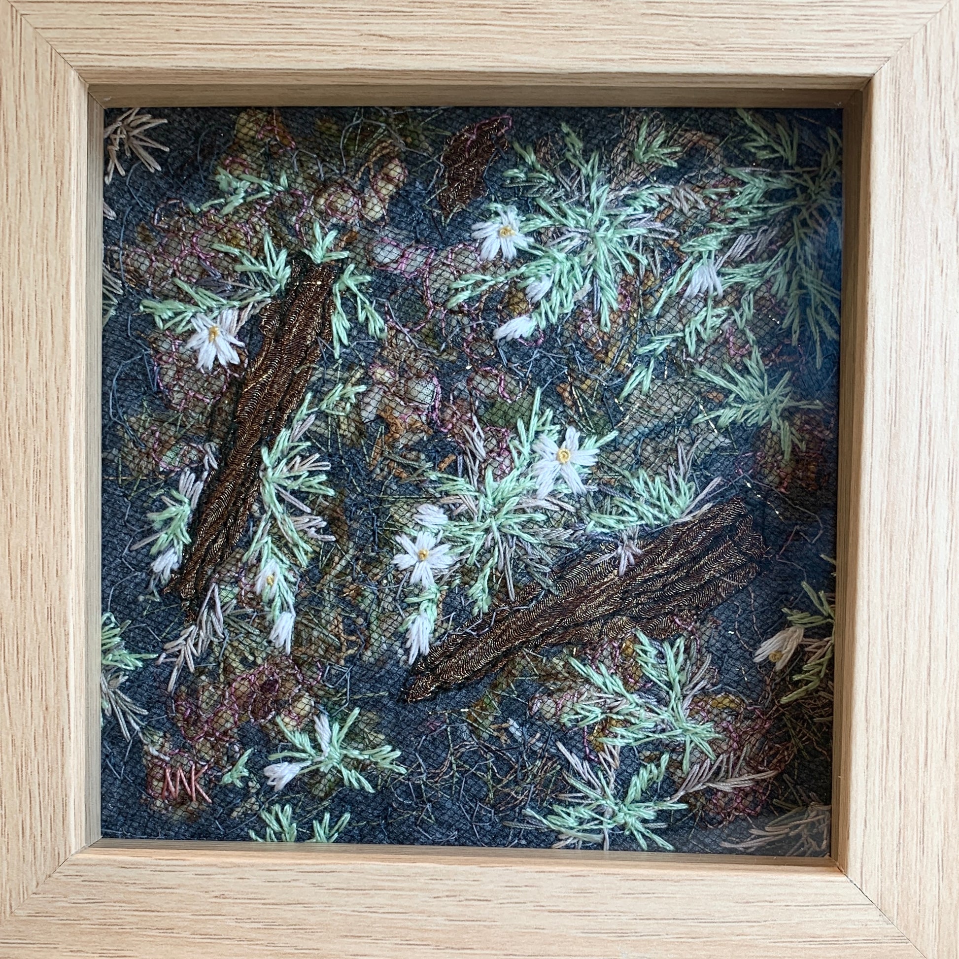 Framed artwork of green embroidered plants and flowers