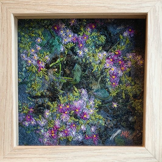 Framed artwork of embroidered purple flowers and green leaves