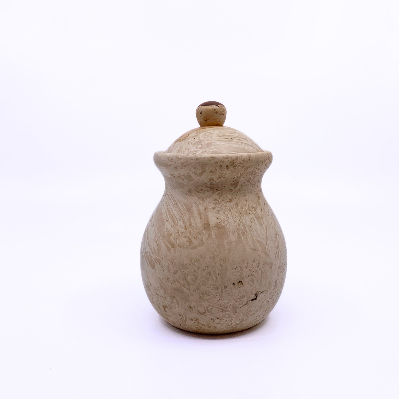 A small handmade wooden lidded jar with a round body and a textured, speckled beige finish, set against a plain white background.