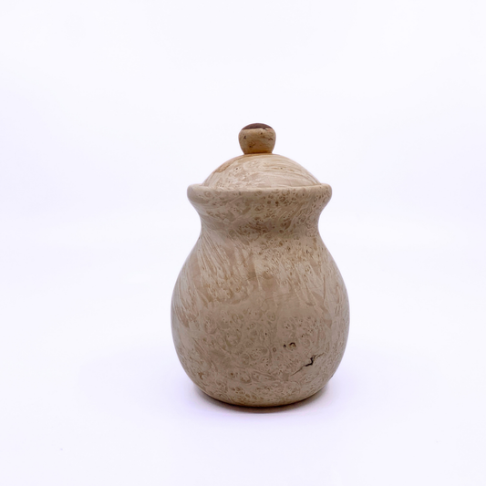 A small handmade wooden lidded jar with a round body and a textured, speckled beige finish, set against a plain white background.