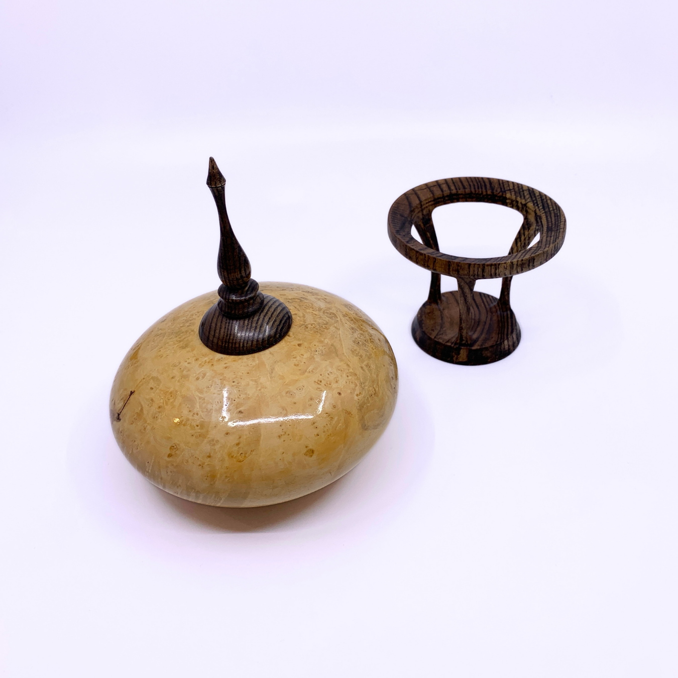A small decorative object with a smooth, rounded beige wood body and a dark brown pointed top, shown next to a matching dark brown ring-shaped stand on a plain white background.