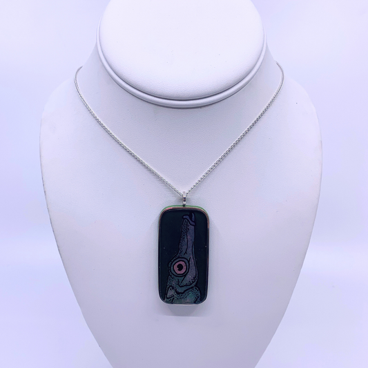 A silver chain necklace with a rectangular pendant featuring a black background and a stylized dish design in pink, red, and green, displayed on a white neck mannequin.