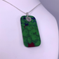 A rectangular pendant necklace with a green and red marbled pattern, hanging from a silver chain on a white mannequin bust.