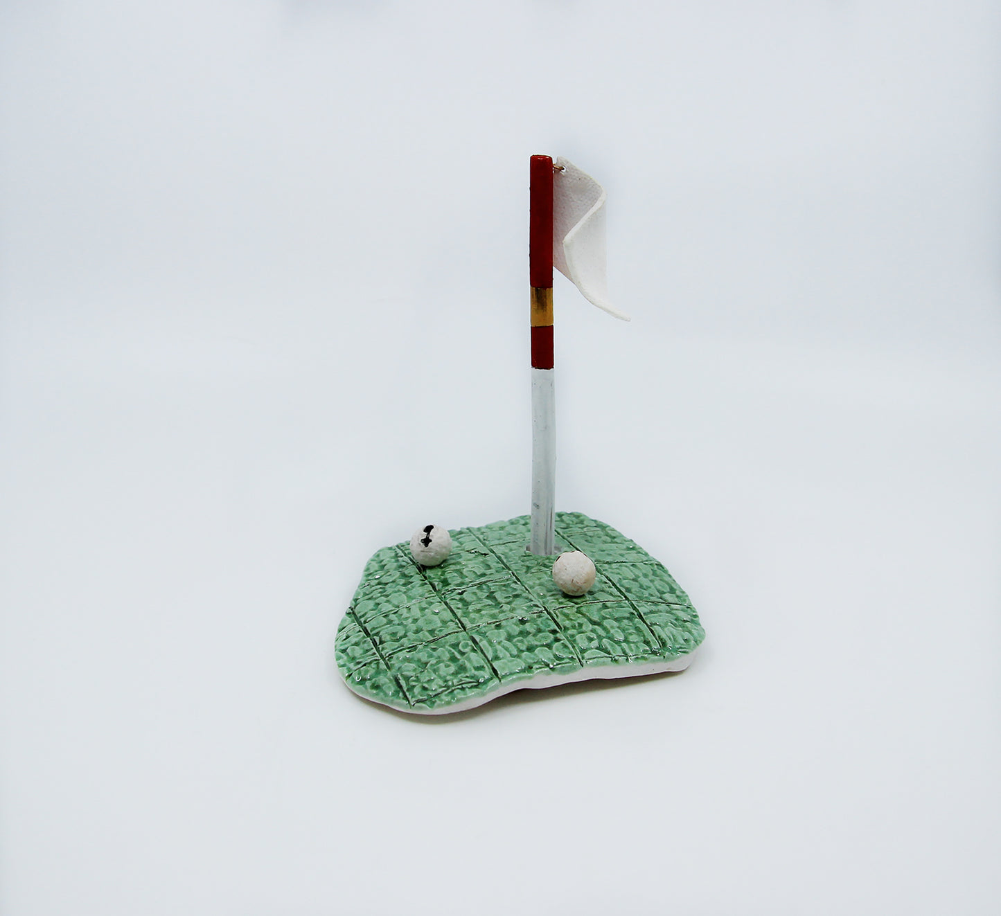 Clay golf green with red flag and two golf balls 