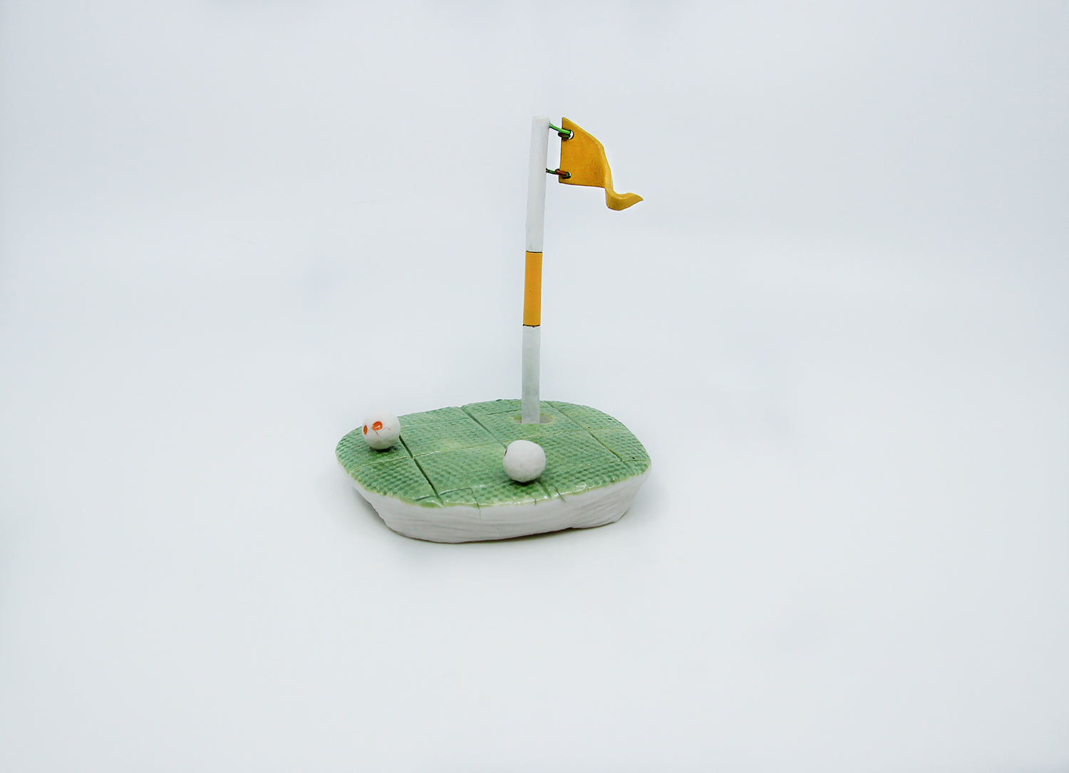 Clay golf green with yellow flag and two golf balls 