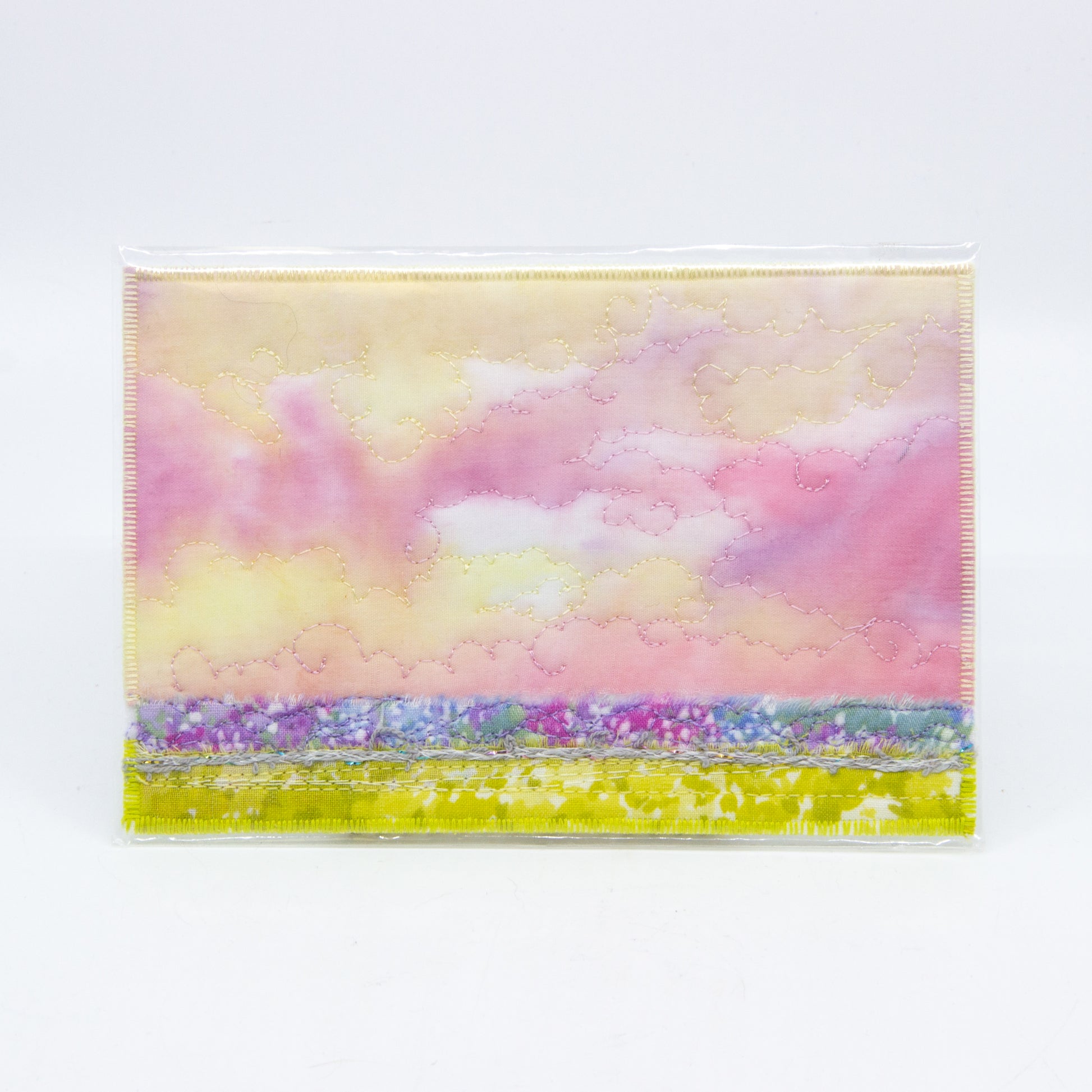 Mini art quilt of a prairie: pink and yellow sky with purple and green fields 